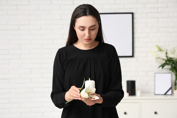 Young woman with funeral lily flower and burning candle in room