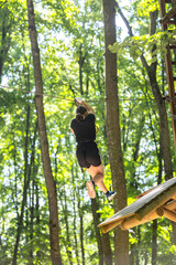Child with harness crossing a rope bridge in a fun adventure park for kids. Outdoor forest activity...