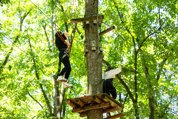 Child with harness crossing a rope bridge in a fun adventure park for kids. Outdoor forest activity...