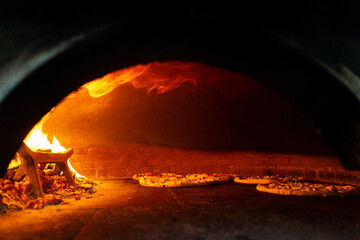 Pizzas baking inside a hot wood-fired oven. Open flames and rustic interior highlight traditional...