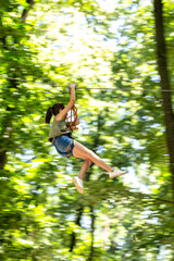 Child with harness crossing a rope bridge in a fun adventure park for kids. Outdoor forest activity...