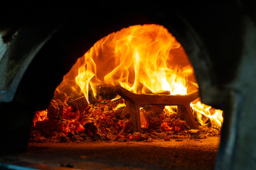 Close-up of flames and glowing embers inside a traditional wood-fired oven. Rustic cooking heat in...
