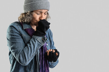 Mature homeless woman coughing on light background