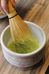 A traditional bamboo whisk (chasen) stirring vibrant green matcha tea in a ceramic bowl, showcasing...