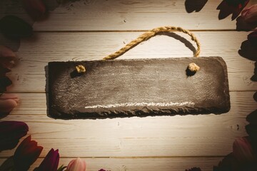 Flat design slate sign with frayed rope handle is lying on whitewashed planks with tulip border