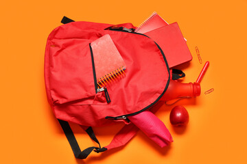 Backpack with school supplies, bottle of water and red apple on orange background. Top view