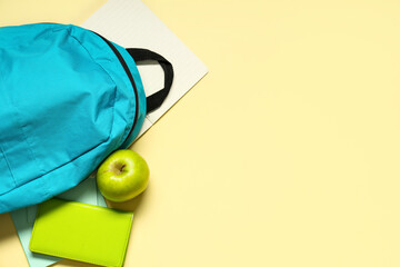 Backpack with green apple and notebooks on yellow background. Top view