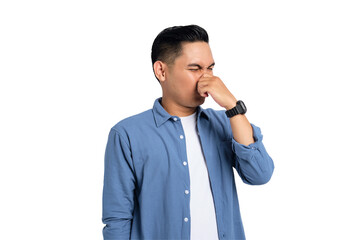 Young Asian man in casual shirt holding breath with finger on nose, smelling something stinky and...