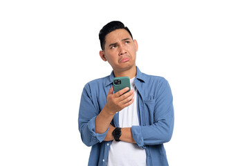 Pensive young Asian man in casual shirt holding smartphone, looking aside at copy space, thinking...