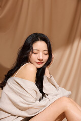 Naklejka premium ベージュの布地背景で撮影をした若い女性の高級感のある美容ポートレート