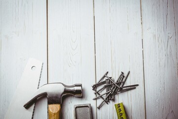 Flat illustration showing claw hammer with wooden handle beside hand saw, nails, tape, copy space