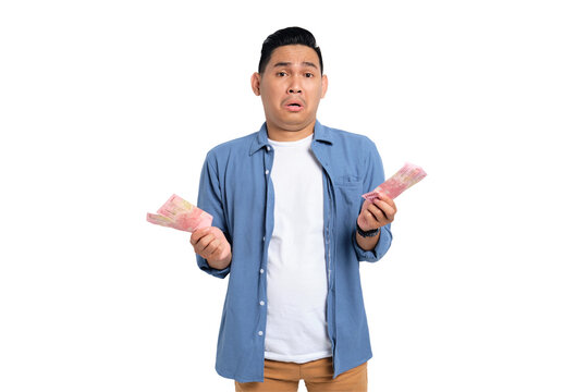 Surprised young Asian man in casual shirt holding money and looking at camera with confused expression isolated on transparent background
