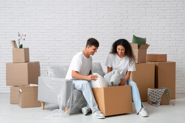 Young happy couple unpacking belongings and sitting on sofa near cardboard boxes in their new flat