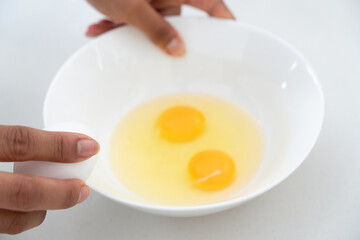 Photograph of a woman's hands holding a plate of eggs about to break an egg on a white surface