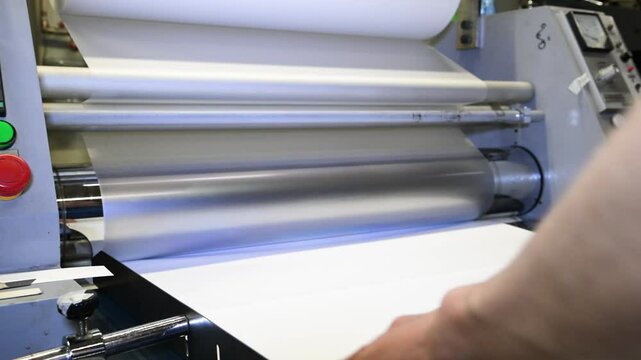 An industrial laminator works by laminating, applying a transparent film to paper in the production room of a printing house