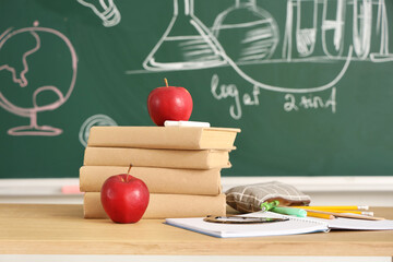 School desk with apples, books, stationery and notebook in light classroom