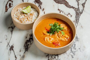 A vibrant bowl of shrimp curry sits next to a dish of coconut rice, garnished with lime