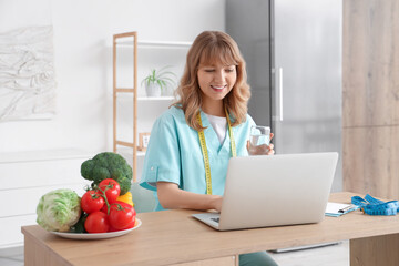 Female nutritionist working with laptop at table in kitchen