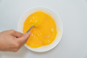 Photograph of a Latina woman's hands beating eggs on a white plate in overhead view
