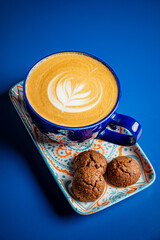 A vibrant blue backdrop showcases a creamy latte with intricate art beside three delectable cookies