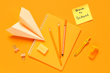 Paper airplane, sticky note with text BACK TO SCHOOL and different stationery on orange background
