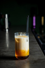 A vibrant drink showcases rich layers of cream and amber hues at a trendy bar setting