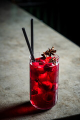 A tall glass of rich crimson drink filled with ice, garnished with aromatic star anise and berries