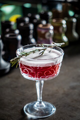 Bright red concoction garnished with a sprig of rosemary captivates in a chic bar atmosphere