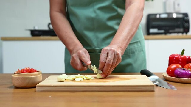 Closeup of hands slicing fresh garlic on a wooden cutting board in kitchen. Perfect for cooking, food prep, healthy eating, herbs