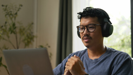 Asian man working from home wearing headphones online meeting.