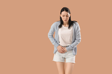 Young woman suffering from severe abdominal pain on beige background