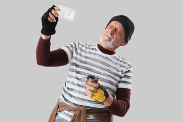 Mature homeless man with dollar banknote and cup on light background