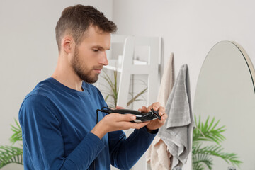 Young man attaching comb to electric trimmer at home