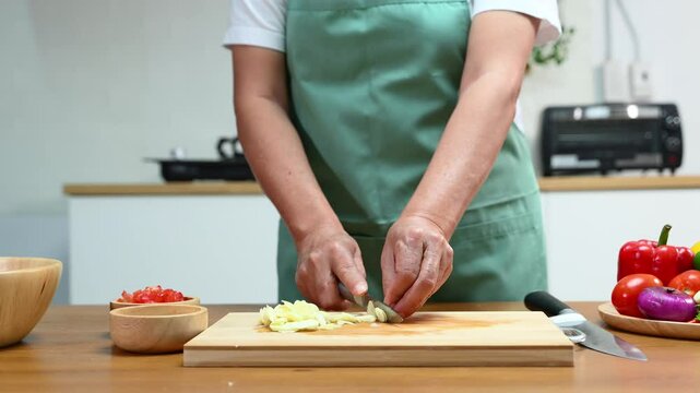 Closeup of hands slicing fresh garlic on a wooden cutting board in kitchen. Perfect for cooking, food prep, healthy eating, herbs