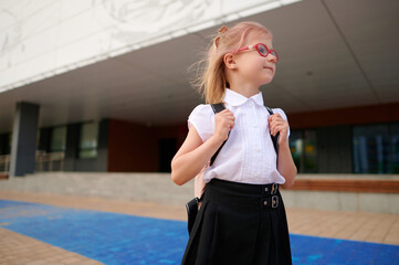 schoolgirl with backpack stands confidently outside modern school building, ready for first day....