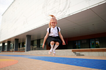 joyful schoolgirl jumping outdoors, wearing glasses, uniform, backpack, embodying excitement and...