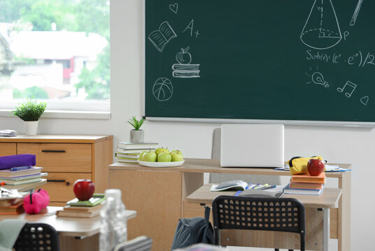 Apples with books and laptop on teacher's desk in classroom
