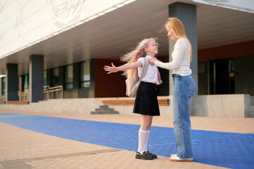 schoolgirl excited for school, arms wide, standing outside modern building, backpack on,...