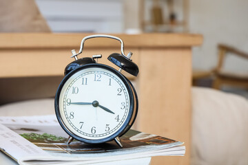 Black alarm clock on magazine in room. Closeup