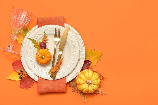 Beautiful table setting with fresh pumpkins and autumn leaves on orange background