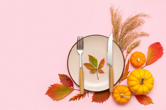Beautiful table setting with fresh pumpkins, wheat and autumn leaves on pink background