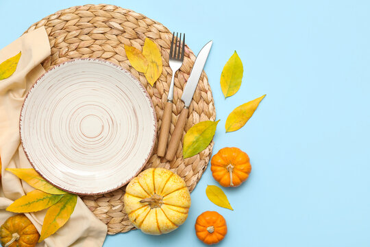 Beautiful table setting with fresh pumpkins and autumn leaves on blue background