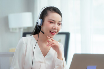 Asian woman wearing headset works at her desk in home office, engaging in online customer service...