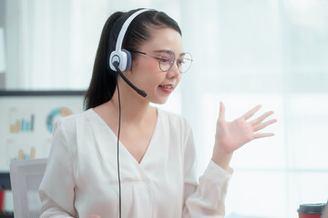 Asian woman wearing headset works at her desk in home office, engaging in online customer service...