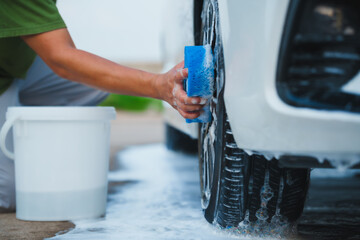 A middle-aged Asian man carefully washes his car using water and foam. Each step from high-pressure...