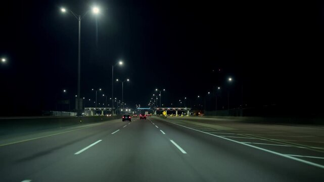 POV shot, driving on the empty illuminated highway with tolls during the night. Cars, trucks on the road. Chicago, IL. 22 August 2024