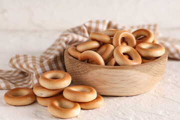 Wooden bowl of tasty bagels on light background