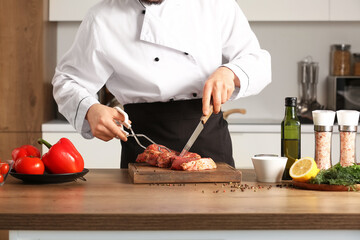 Male chef cutting raw meat at table in kitchen