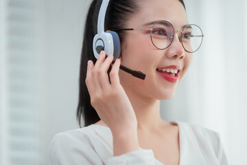 Asian woman wearing headset works at her desk in home office, engaging in online customer service...