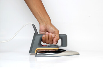 Fototapeta premium A hand firmly grasps a classic dry iron, ready for pressing clothes, against a clean white background